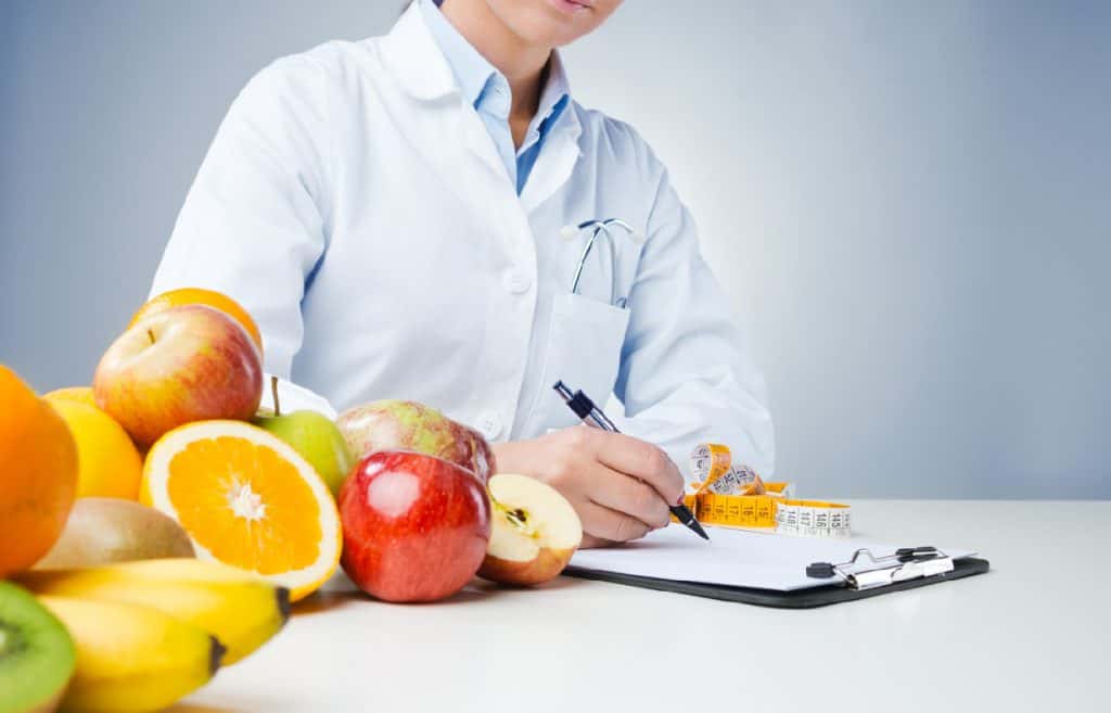 Masanın üzerinde meyveler ve diyet yazan bir kadın diyetisyen